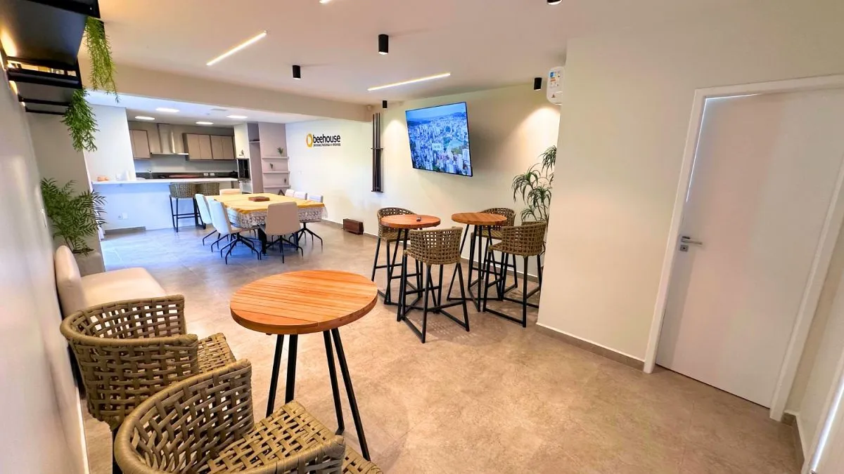 Espaço de convivência da Beehouse, com mesas e copa ao fundo.